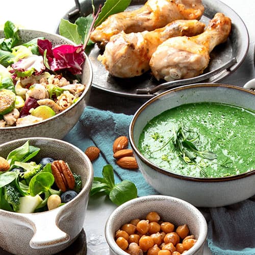 Platos con ensalada, legumbres, crema de verduras y pollo.